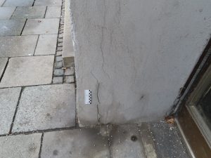 Exemplarische Rissbildungen im Sockelbereich einer Fassade, die anhand von Fotoaufnahmen dokumentiert sind.